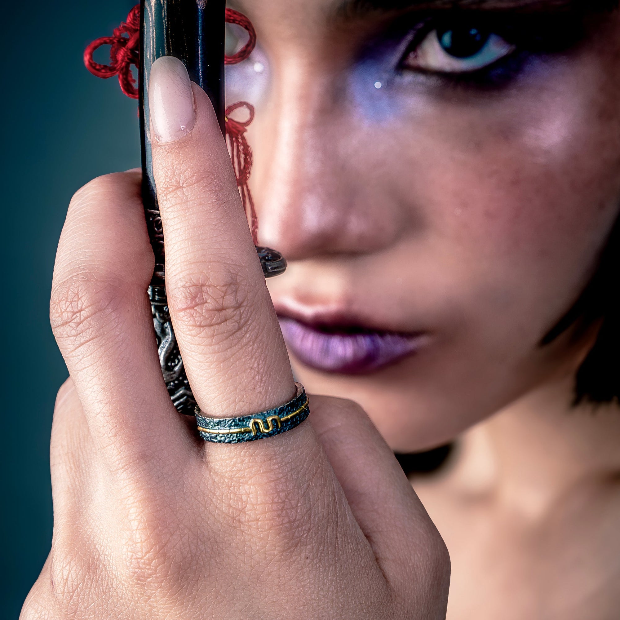 [full] Close-up of a hand wearing a statement silver ring holding a decorative object near a person's face against a dark background