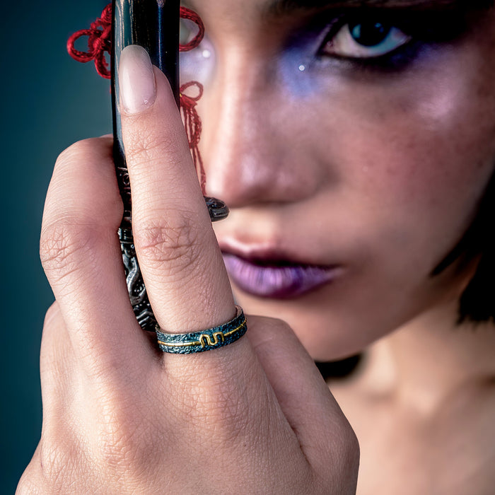 [full] Close-up of a hand wearing a statement silver ring holding a decorative object near a person's face against a dark background