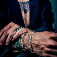 [full] Close-up of a person's tattooed hands with rounded curb link bracelet in sterling silver with rugged gun-metal finish.
