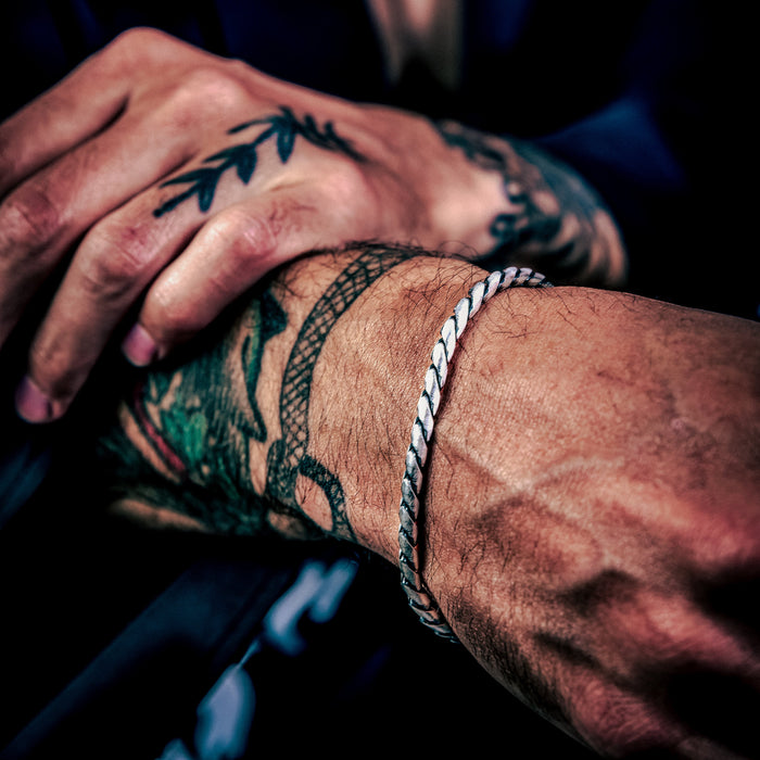 [full] Close-up of a person's tattooed hands with rounded curb link bracelet in sterling silver with rugged gun-metal finish.