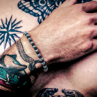 [full] Person with tattoos on arm and chest wearing sterling silver bracelet with star-engraved beads and black cord detailing.