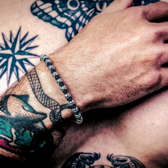 [full] Person with tattoos on arm and chest wearing sterling silver bracelet with star-engraved beads and black cord detailing.