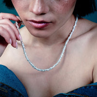 [full] - Person wearing a delicate silver necklace against a dark background