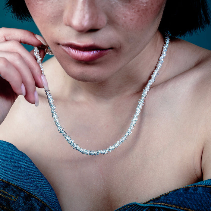 [full] - Person wearing a delicate silver necklace against a dark background