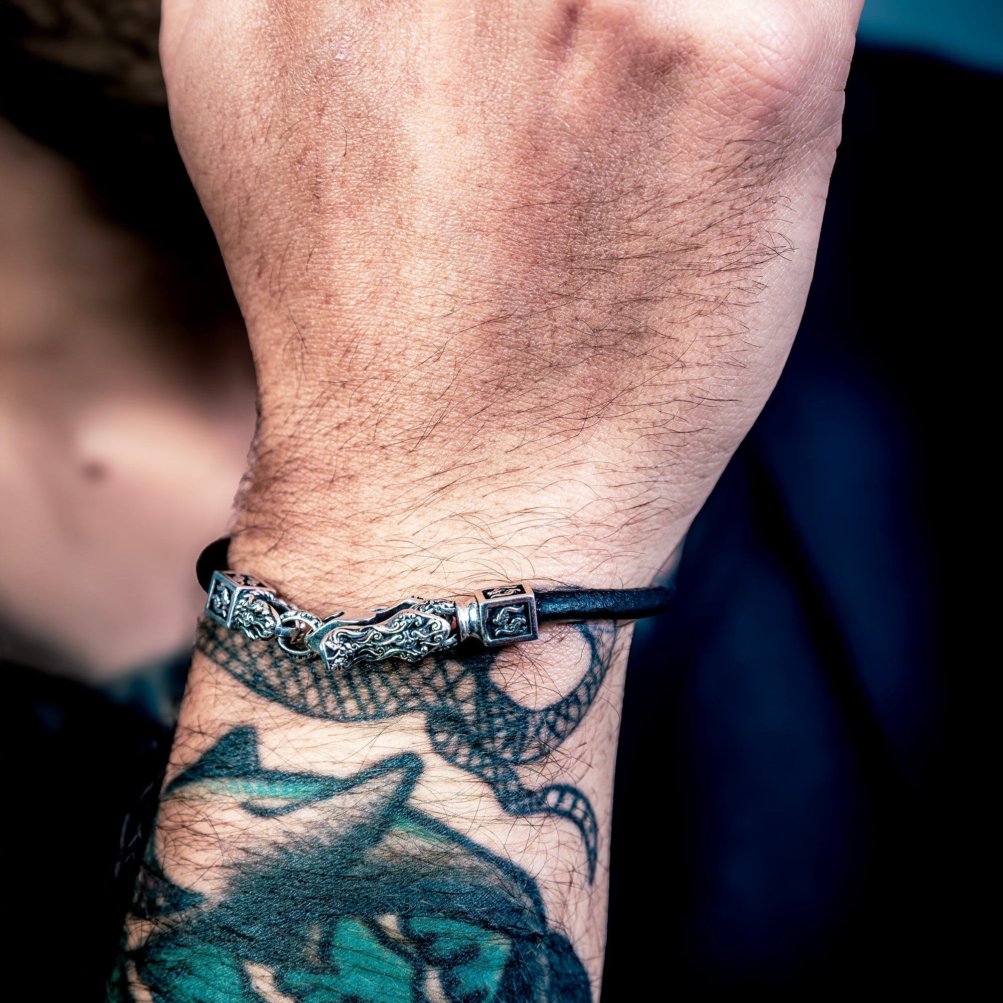 [full] Close-up of a person's hands with tattoos and a sterling silver bracelet on a dark background