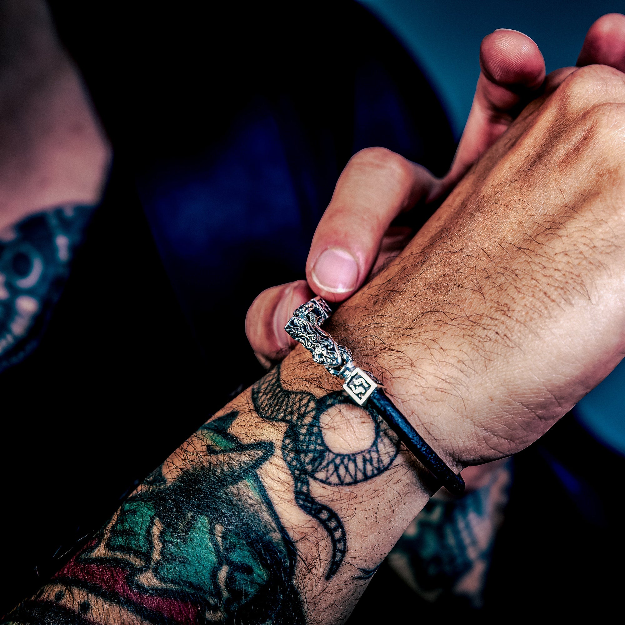 [full] Close-up of a person's hands with tattoos and a sterling silver bracelet on a dark background