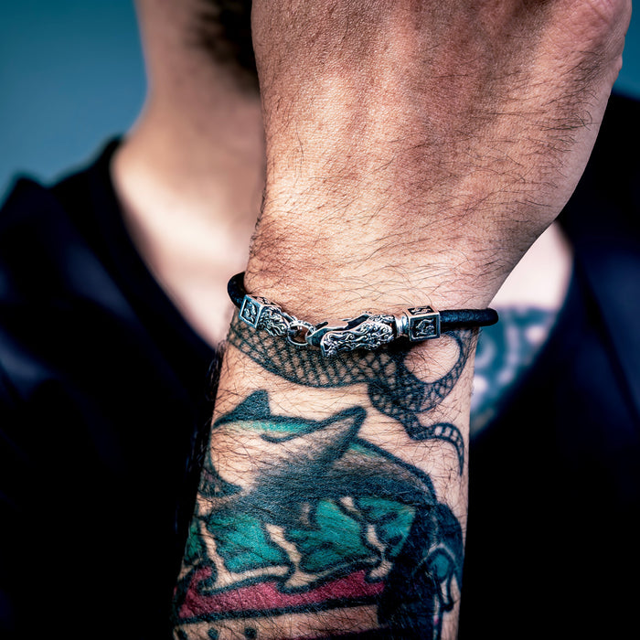 [full] Close-up of a person's hands with tattoos and a sterling silver bracelet on a dark background