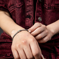 [full] Close-up of a person wearing a silver and ruthenium bracelet with a dark background