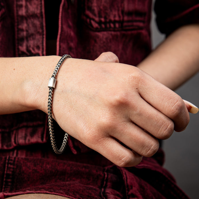 [full] Close-up of a person wearing a silver and ruthenium bracelet with a dark background