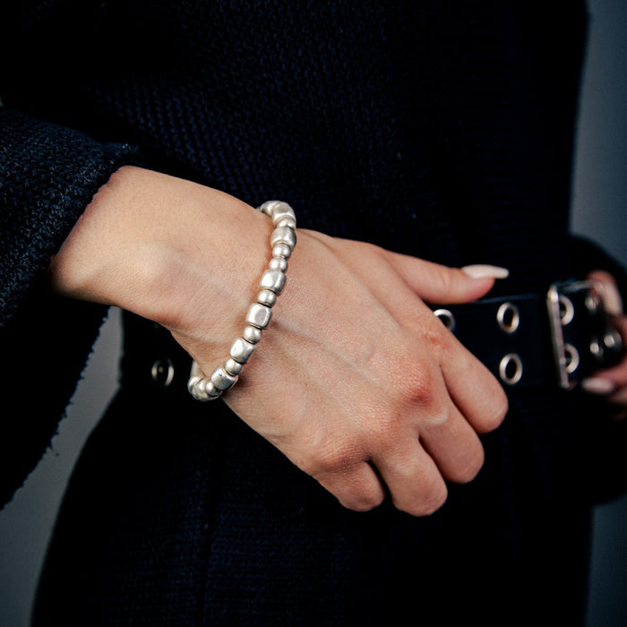 [full] - Hand wearing a black coat with a belt and 999 Silver bracelet on a dark background