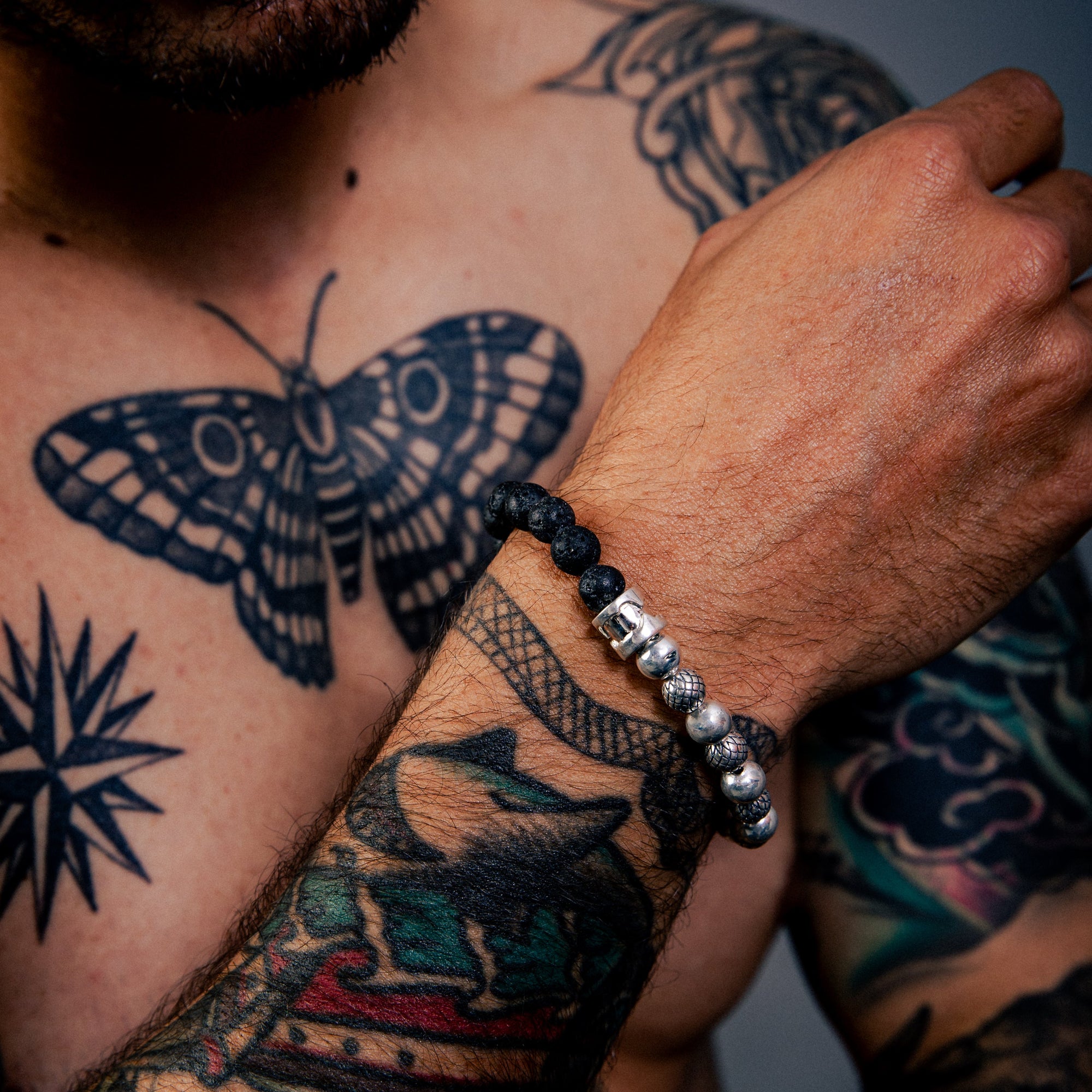 [full] Person with tattoos on chest and arms wearing black lava stone and sterling silver bead bracelet with contrasting textures.