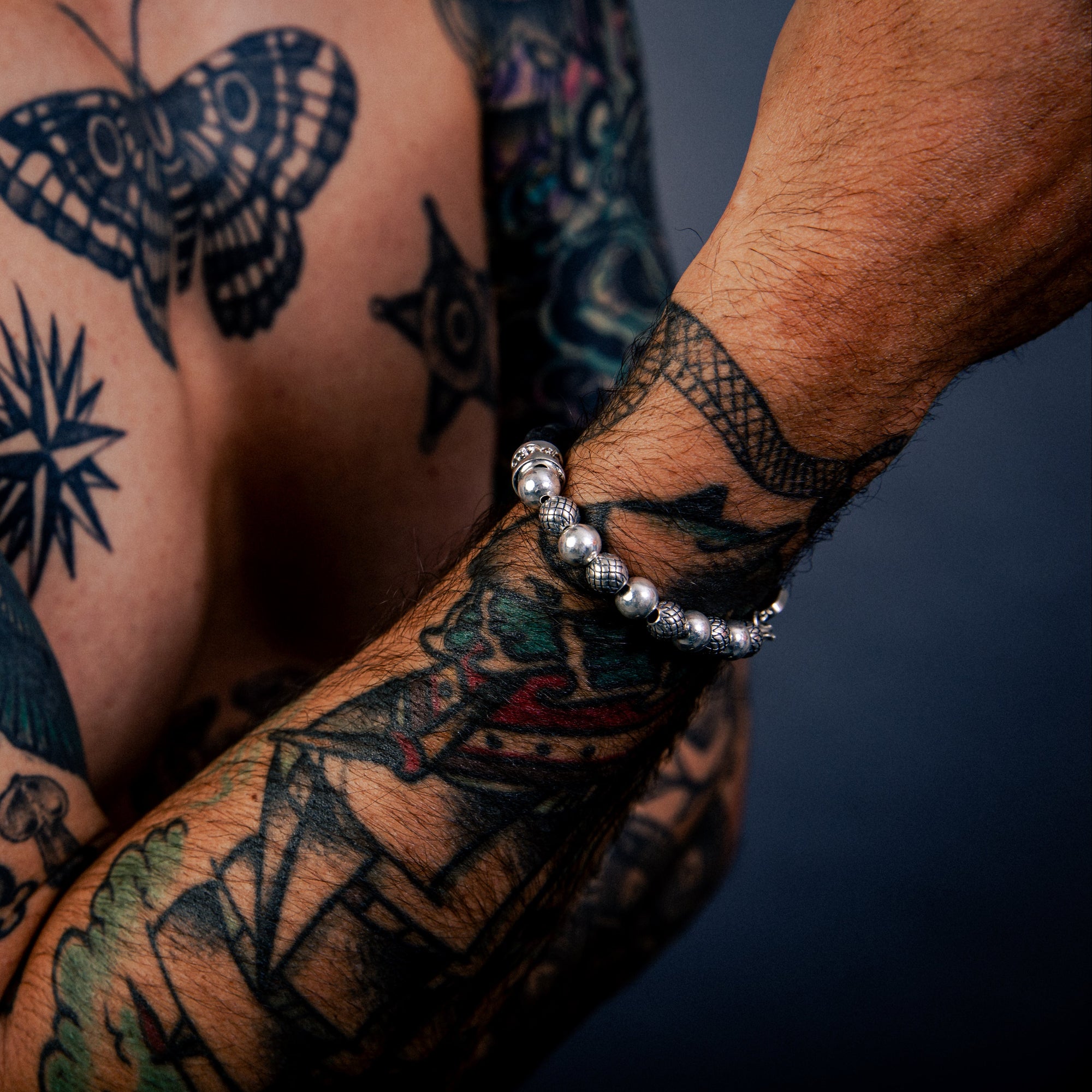 [full] Person with tattoos on chest and arms wearing black lava stone and sterling silver bead bracelet with contrasting textures.