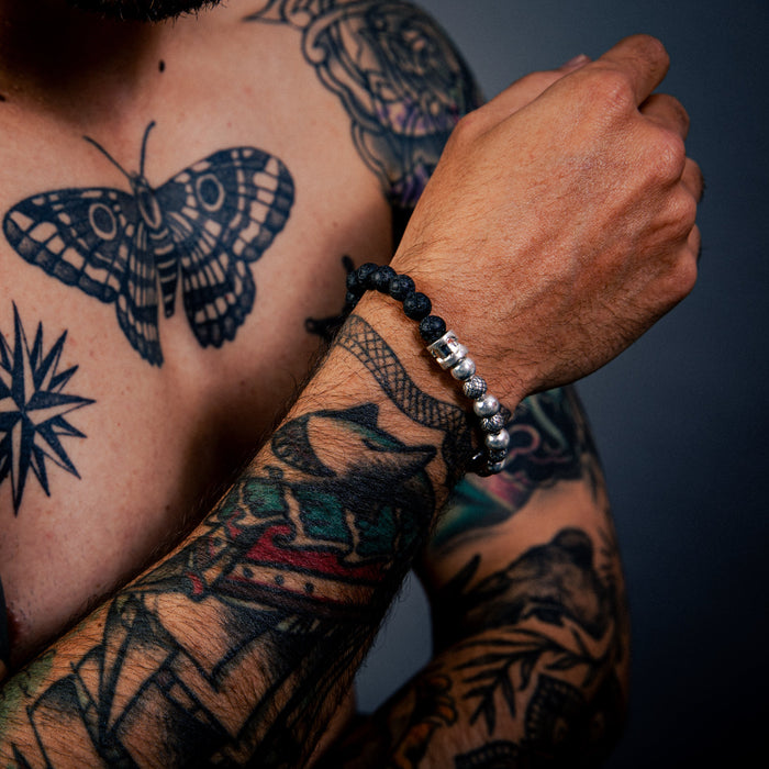 [full] Person with tattoos on chest and arms wearing black lava stone and sterling silver bead bracelet with contrasting textures.