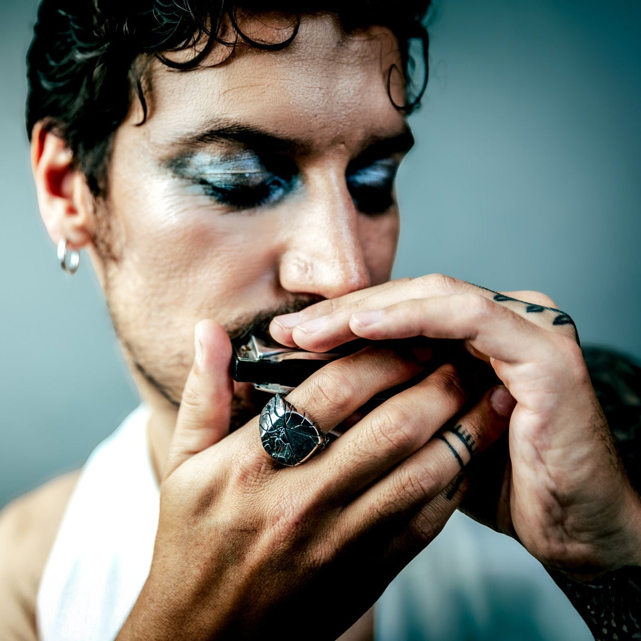 [full] Man wearing a sterling silver ring, playing a harmonica with a dark background