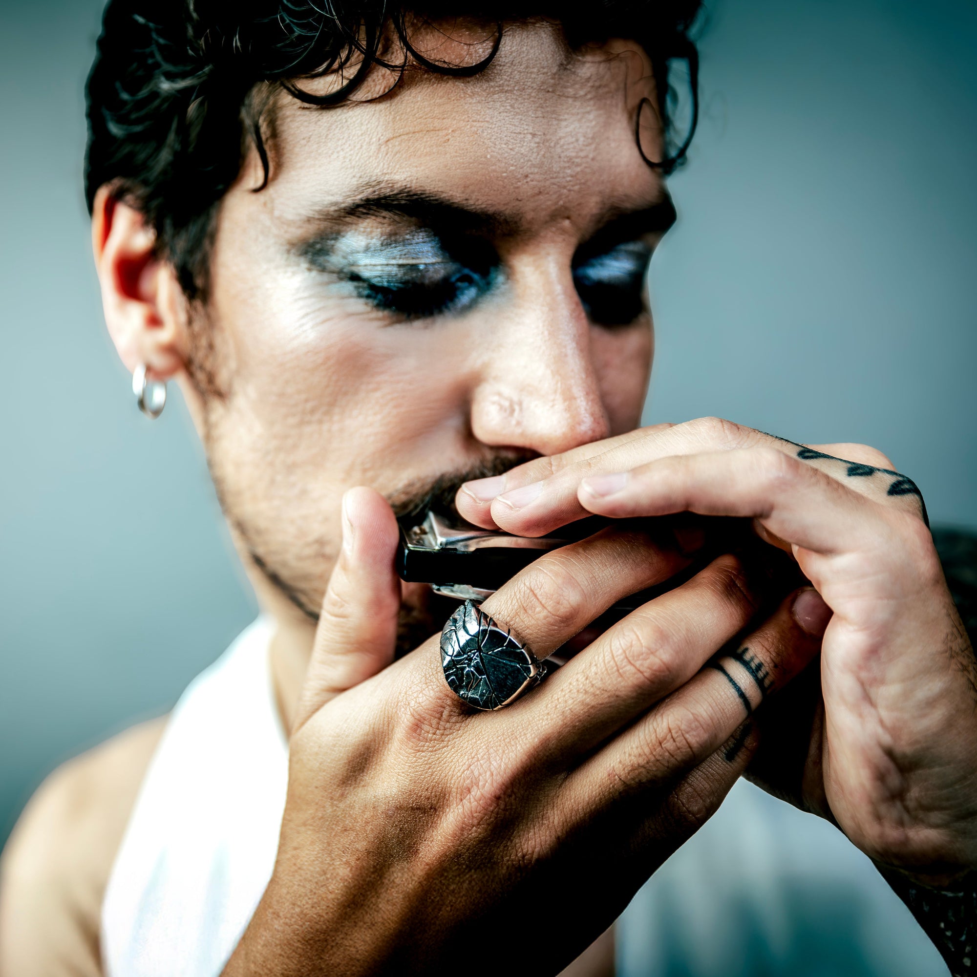 [full] Man wearing a sterling silver ring, playing a harmonica with a dark background