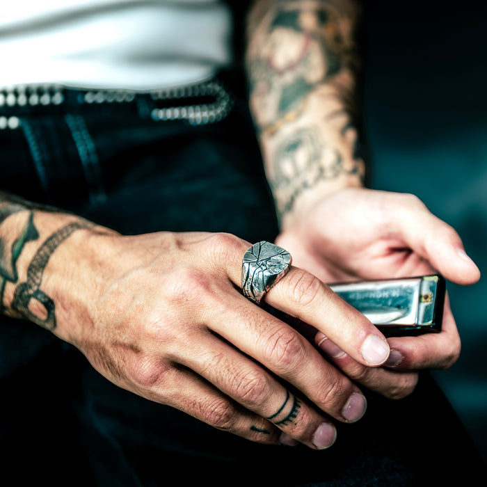 [full] Person holding a harmonica with tattoos and a sterling silver ring on fingers