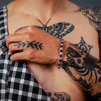 [full] - Person wearing checkered overalls with tattoos and a sterling silver star bead bracelet with black cord and polished finish.