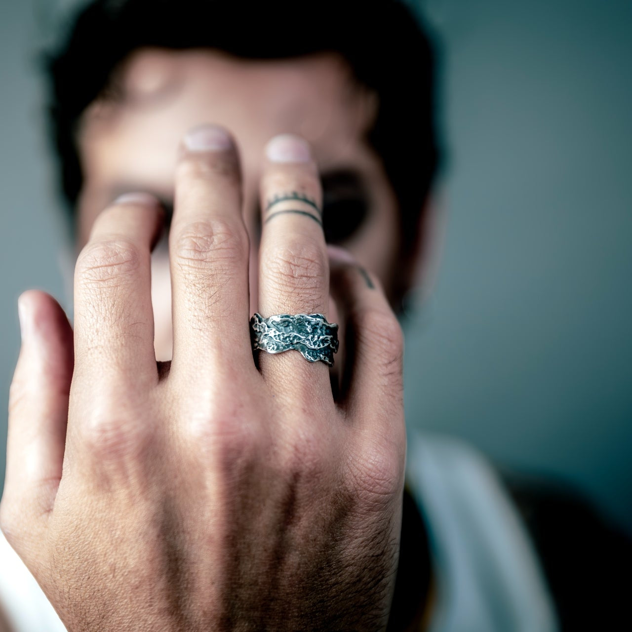 [full] Hand with a sterling silver ring held up to the camera against a blurred background