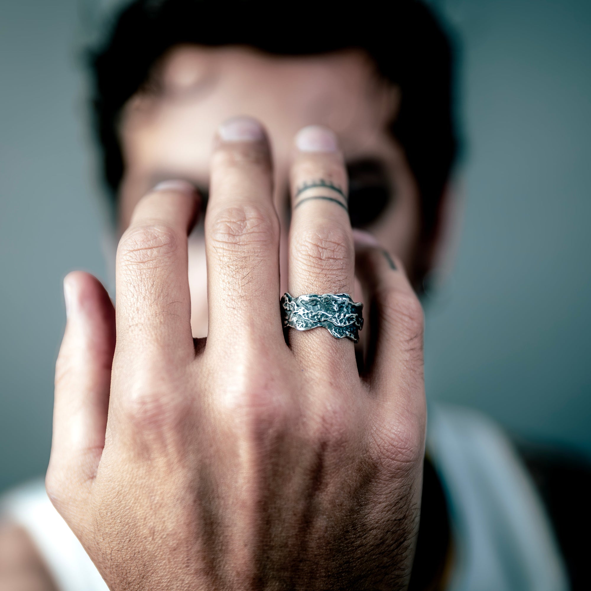 [full] Hand with a sterling silver ring held up to the camera against a blurred background