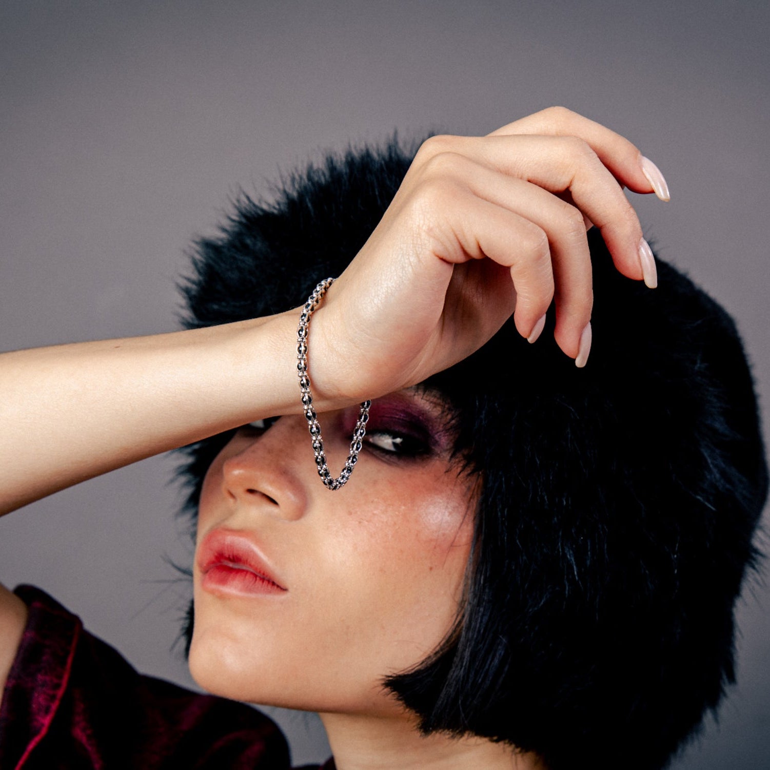 [full] - Person wearing a black fur hat and red garment, with a sterling silver chain bracelet with polished black stones and rhodium finish hanging from the hand.