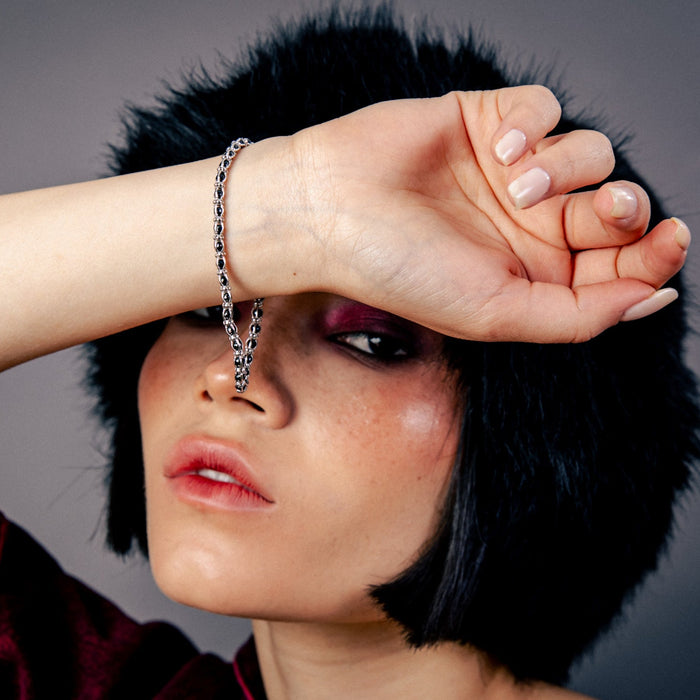 [full] - Person wearing a black fur hat and red garment, with a sterling silver chain bracelet with polished black stones and rhodium finish hanging from the hand.