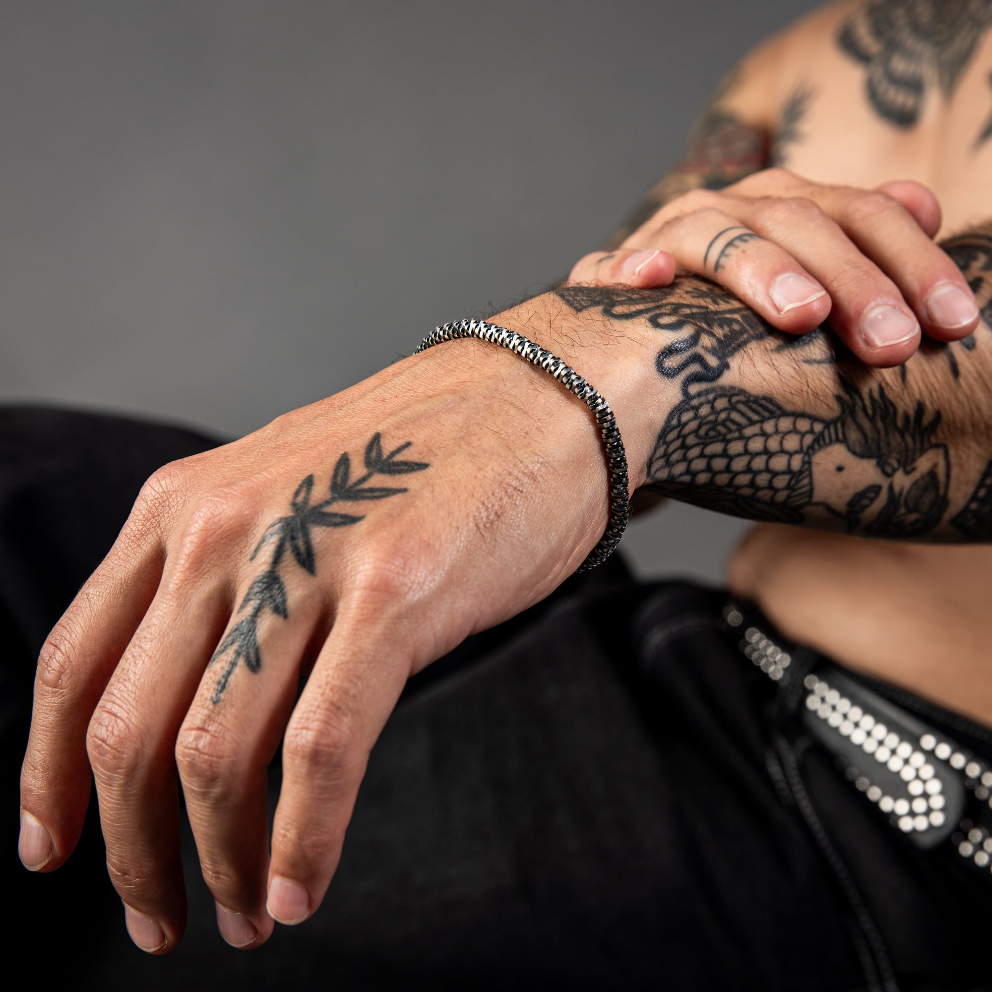 [full] Close-up of tattooed hands with intricate designs wearing a mirror-snake design sterling silver bracelet with dark gun-metal ruthenium plating.
