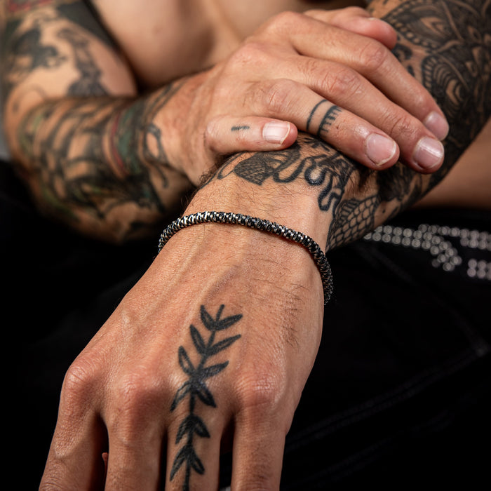 [full] Close-up of tattooed hands with intricate designs wearing a mirror-snake design sterling silver bracelet with dark gun-metal ruthenium plating.
