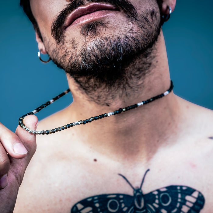 [full]-Man with a butterfly tattoo on his chest holding a beaded sterling silver necklace against a blue background