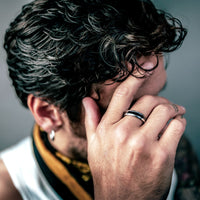 [full] Person with curly hair covering face with hand, wearing a ceramic ring, against a blurred background