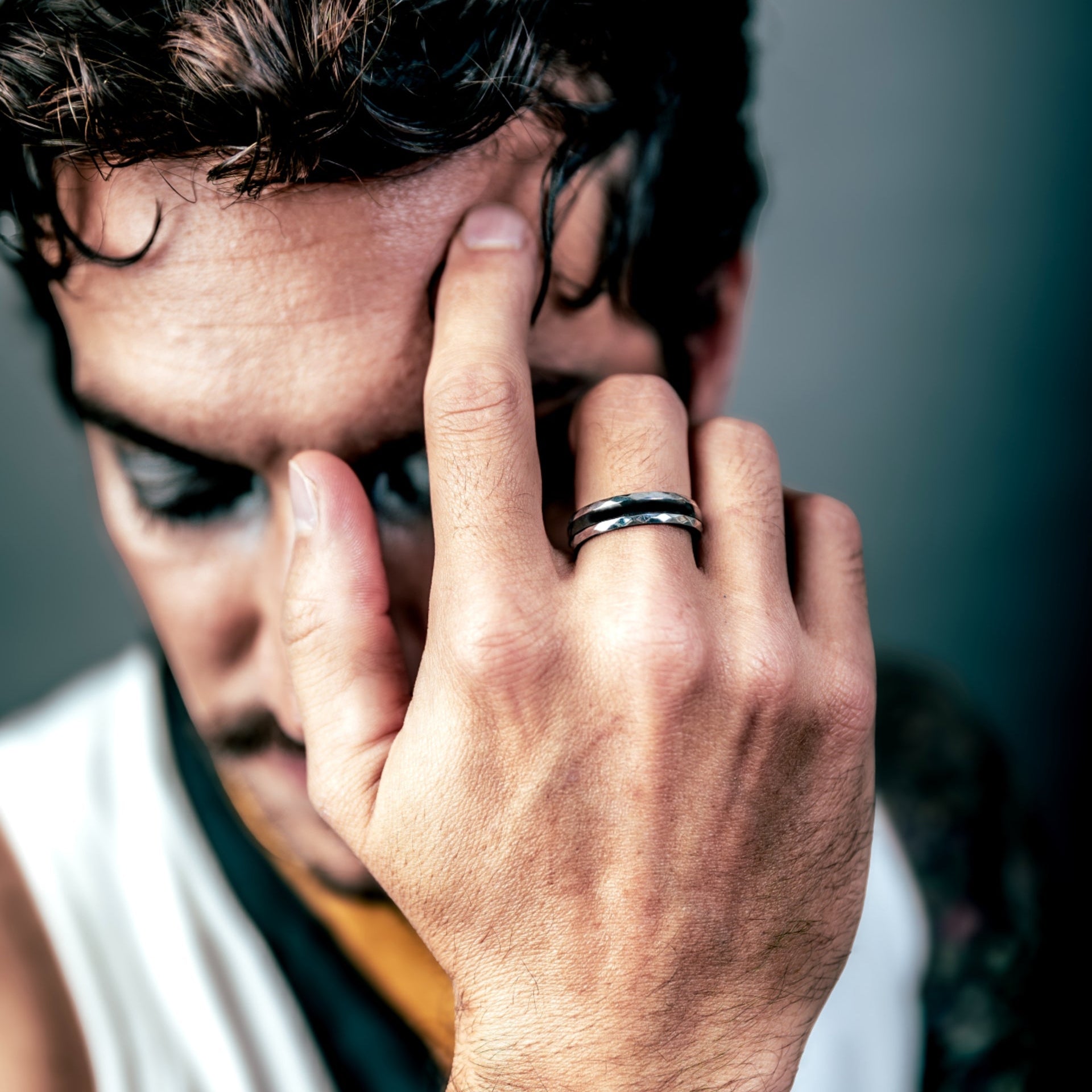 [full] Man with tattooed hand holding head, wearing a ceramic ring