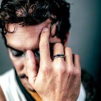 [full] Man with tattooed hand holding head, wearing a ceramic ring