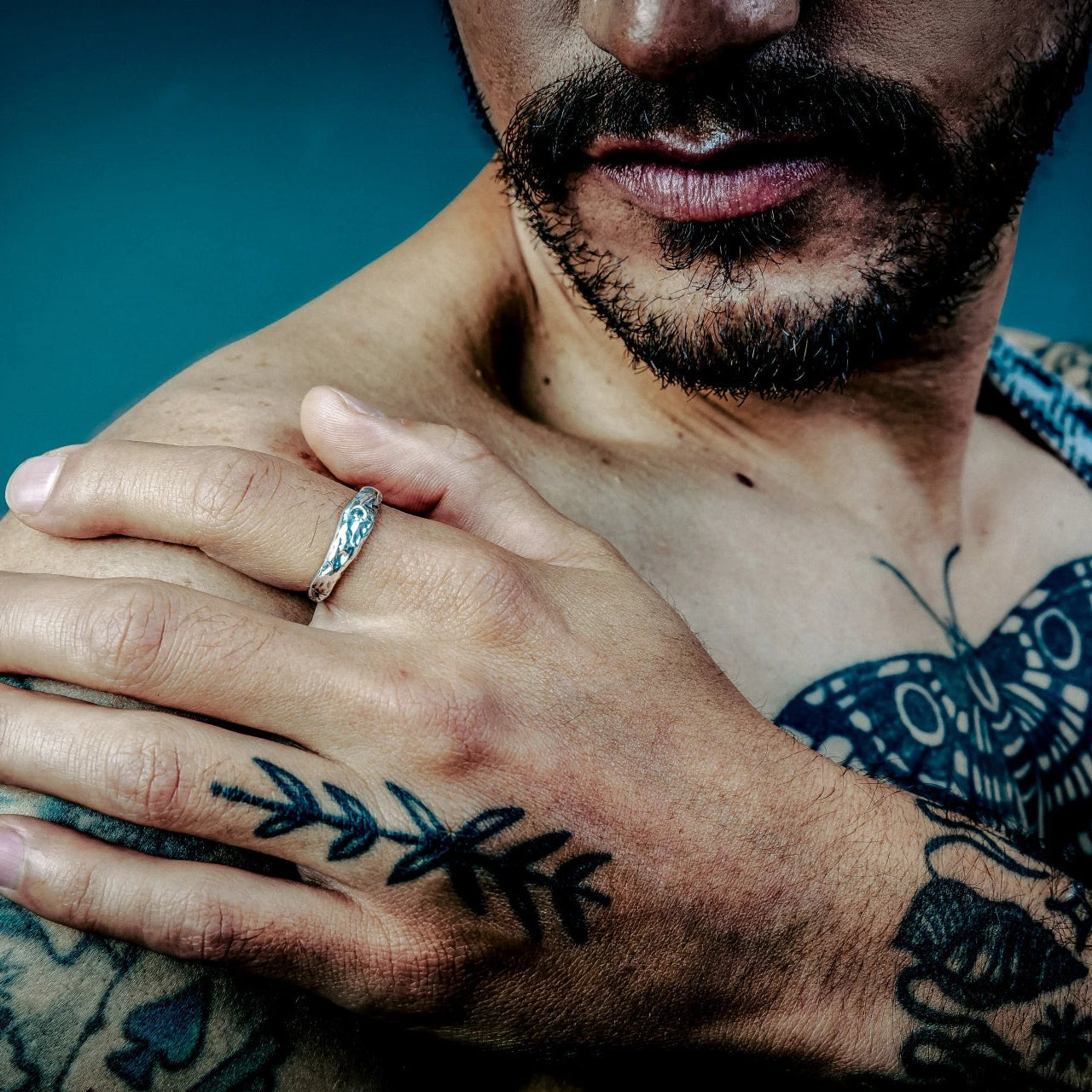 [full] - Man with tattoos with a silver ring against a blue background
