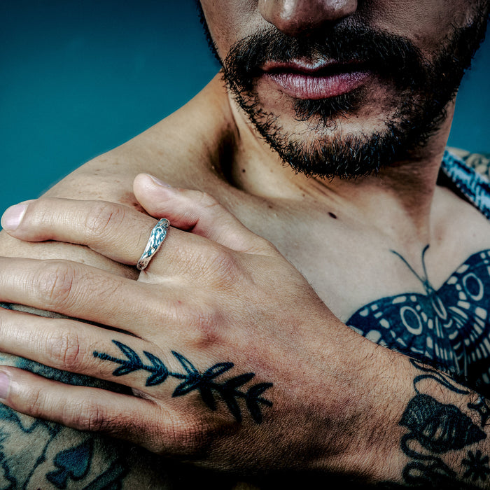 [full] - Man with tattoos with a silver ring against a blue background