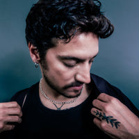 [full] Man with tattoos and jewelry against a dark background