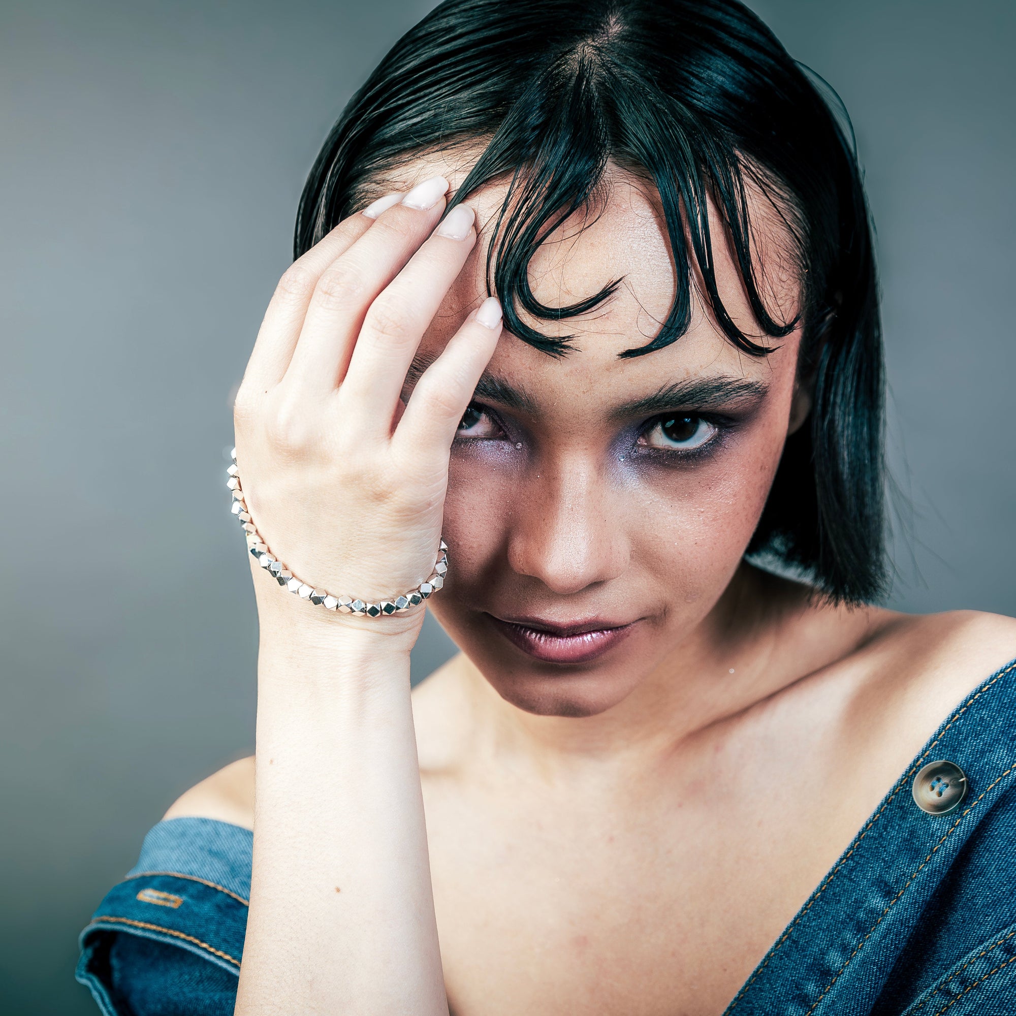 [full] - Woman with dark hair and a denim shirt with faceted sterling silver beads bracelet with geometric design and polished finish.